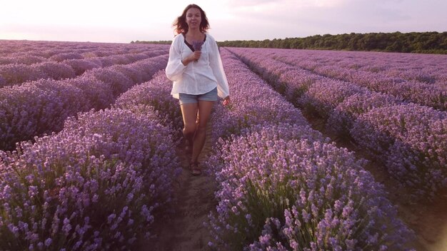 Giovane donna in camicia bianca che cammina nel bellissimo campo di lavanda