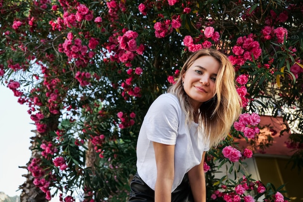 Giovane donna in camicia bianca con trucco naturale in piedi nel cespuglio in fiore