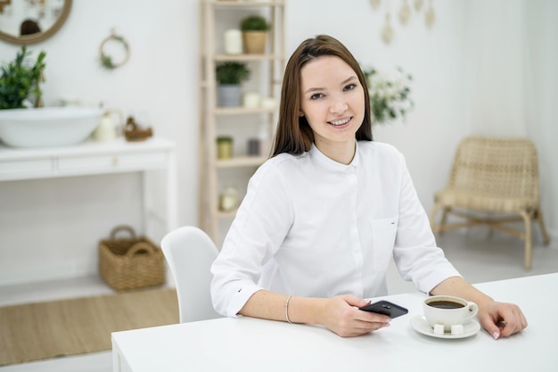 Giovane donna in camicia bianca sta bevendo caffè in un salone di bellezza L'amministratore di una bella ragazza offre da bere al visitatore Il dipendente risponde alle domande per telefono