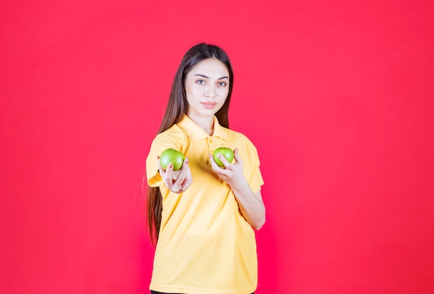 Giovane donna in camicia gialla che tiene in mano una mela verde e ne offre una al cliente