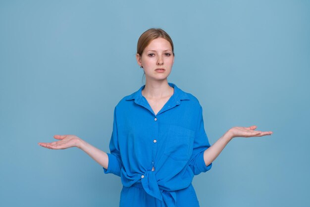 Giovane donna in camicia su sfondo blu che indica di lato con entrambe le mani che mostra qualcosa di strano a...