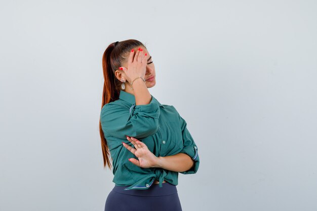 Giovane donna in camicia verde che soffre di mal di testa e sembra stanca, vista frontale.