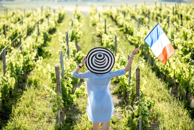 Giovane donna in cappello a strisce con bandiera francese godendo di una splendida vista del tramonto sul vigneto nella regione di Bordeaux in Francia