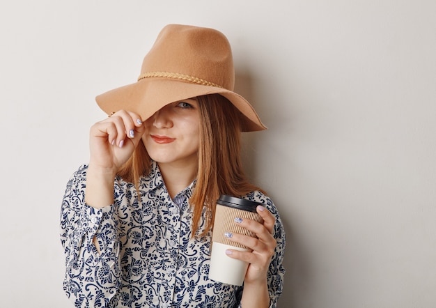 Giovane donna in cappello beige che tiene una tazza di caffè