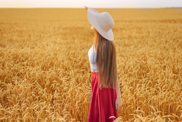 Giovane donna in cappello con bei capelli lunghi su sfondo di grano maturo.