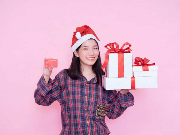 Giovane donna in cappello della Santa che tiene la carta di credito e confezioni regalo sulla parete rosa.