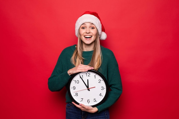 Giovane donna in cappello della Santa con l'orologio sulla parete rossa. Conto alla rovescia per Natale