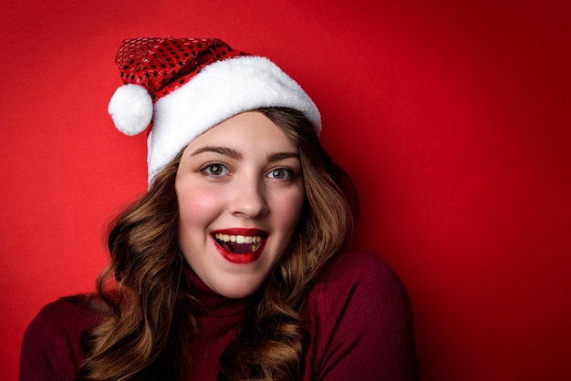 Giovane donna in cappello di Babbo Natale su sfondo rosso. Concetto di Natale e Capodanno.