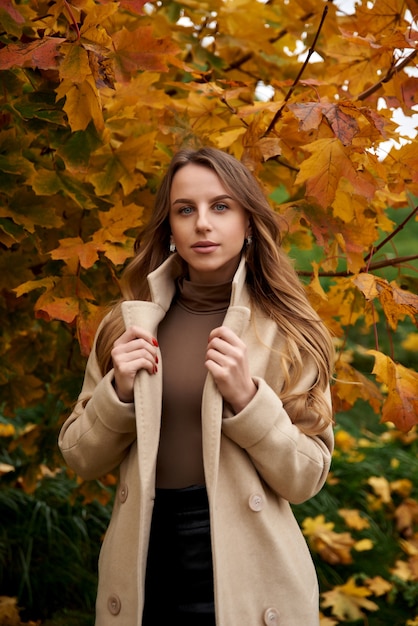 Giovane donna in cappotto in piedi sulla strada in un parco in autunno