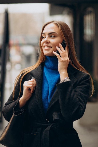 Giovane donna in cappotto nero che usa il telefono