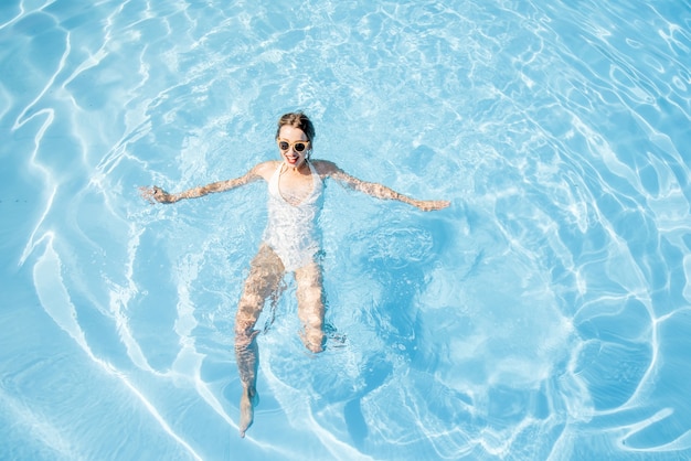 Giovane donna in costume da bagno che nuota nel bacino con acqua blu. Vista generale dall'alto