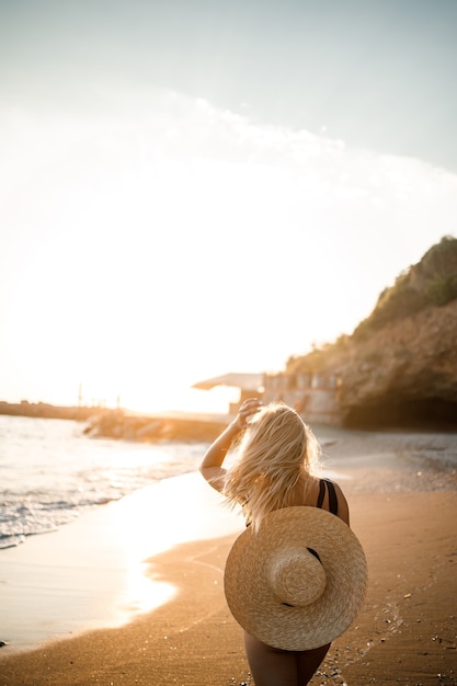 Giovane donna in costume da bagno con una bella figura in riva al mare al tramonto. Messa a fuoco selettiva