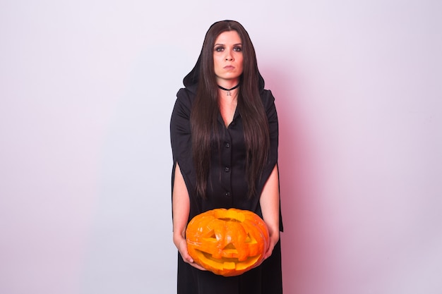 Giovane donna in costume da strega di Halloween in studio con zucca gialla.