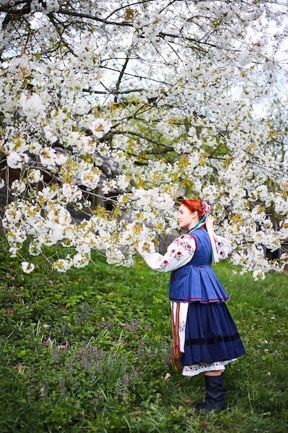 Giovane donna in costume nazionale ucraino Giovane donna sorridente in abiti tradizionali Soggiorno vicino all'albero in fiore Pace in Ucraina