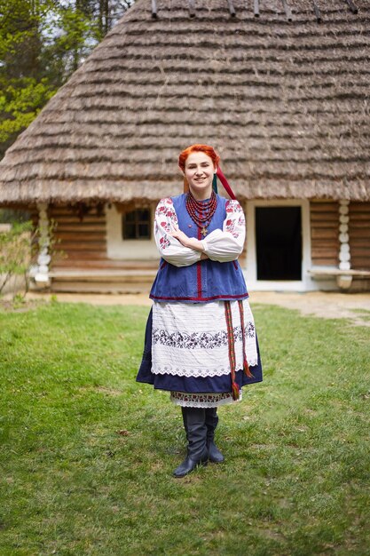 Giovane donna in costume nazionale ucraino Giovane signora sorridente in abiti tradizionali vicino alla vecchia casa di legno Pace in Ucraina