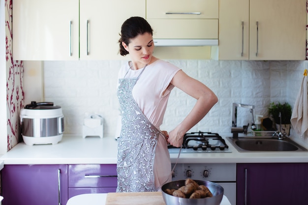 Giovane donna in cucina annodare un grembiule sulla schiena