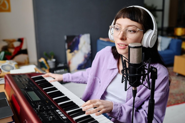 Giovane donna in cuffia che suona il pianoforte e prova la sua nuova canzone in studio