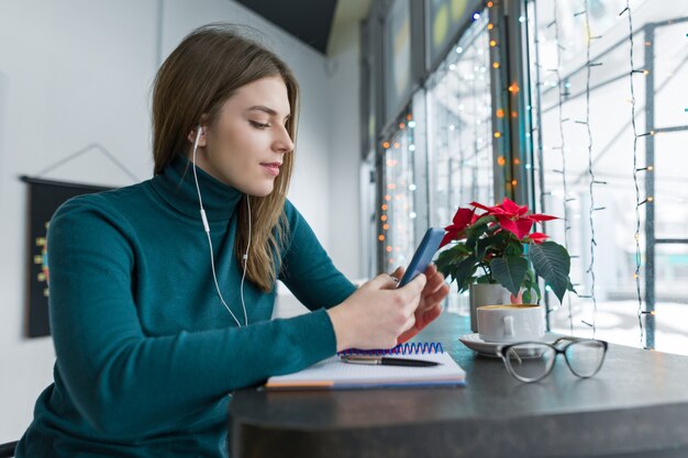 Giovane donna in cuffie facendo uso dello smartphone per lavoro e studio