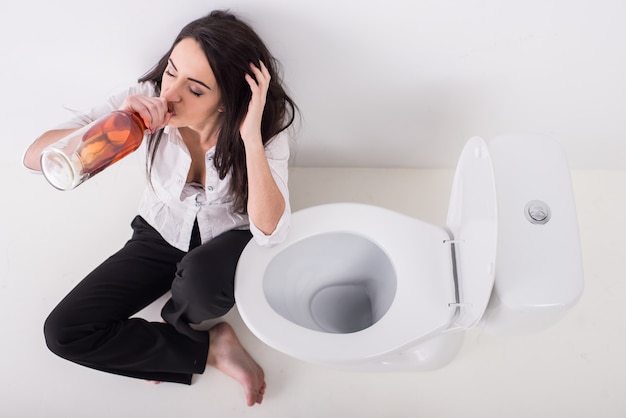 Giovane donna in depressione, sta bevendo alcolici in bagno.