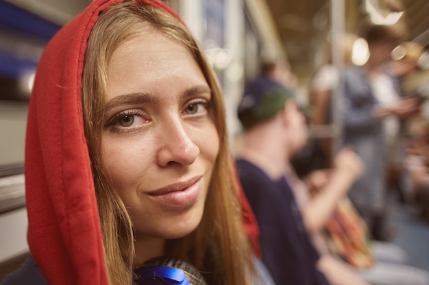 Giovane donna in felpa con cappuccio rossa su sfondo di passeggeri in auto del treno in metropolitana nelle ore di punta.