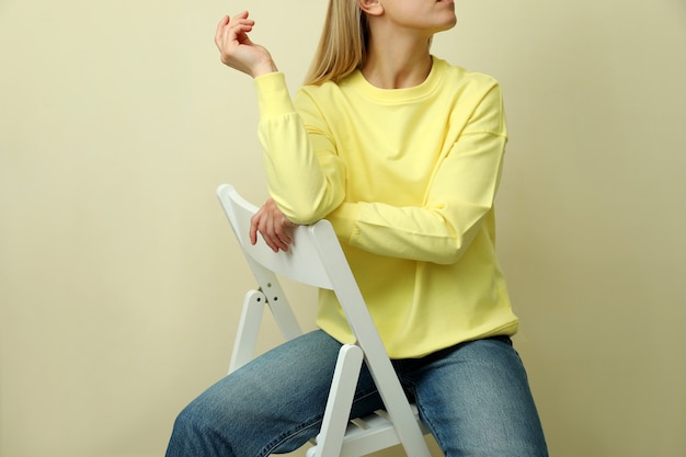 Giovane donna in felpa gialla seduta su sfondo beige