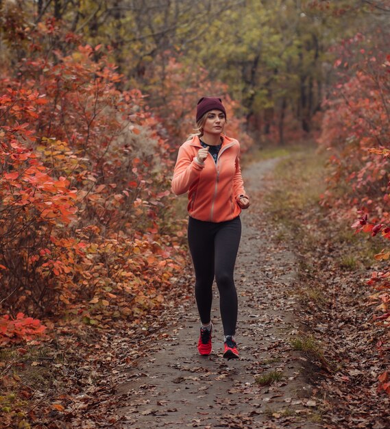 Giovane donna in forma in abbigliamento sportivo corre lungo un sentiero nel bosco con foglie arrossate