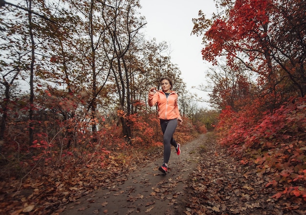 Giovane donna in forma in abbigliamento sportivo corre lungo un sentiero nel bosco con foglie arrossate