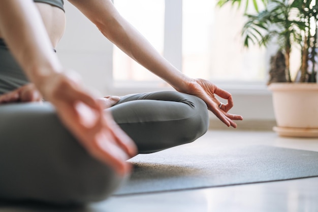 Giovane donna in forma pratica yoga facendo asana posizione del loto in studio di yoga leggero con pianta della casa verde