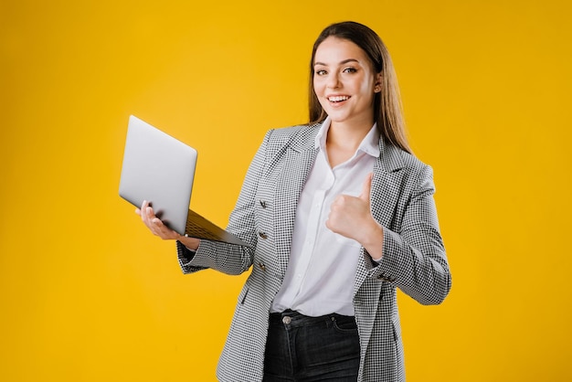 Giovane donna in giacca e camicia che indossa occhiali da vista utilizzando un computer portatile su sfondo giallo