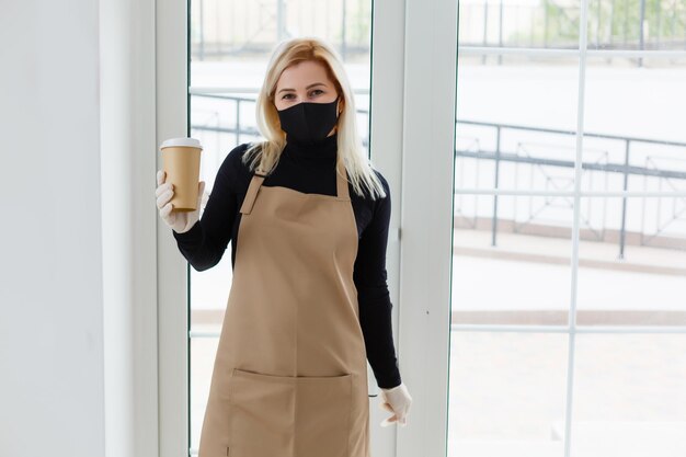 Giovane donna in grembiule con caffè su sfondo grigio. Concetto di barista