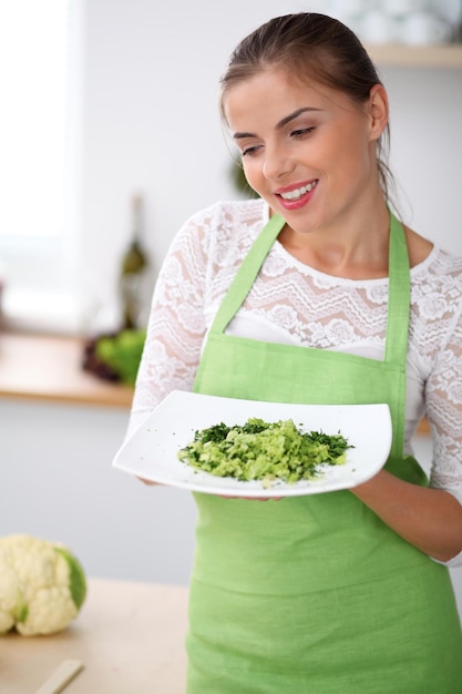 Giovane donna in grembiule verde sta cucinando in una cucina La casalinga offre insalata fresca