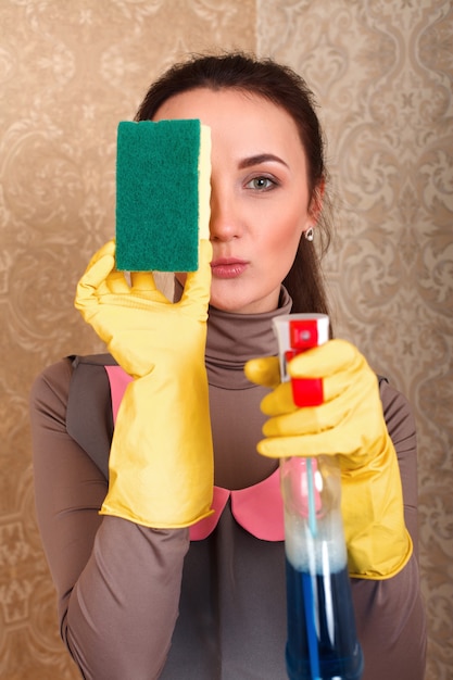 Giovane donna in guanti di gomma con spugna di lavaggio e detergente. Concetto di pulizia