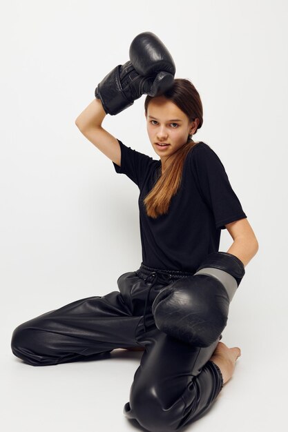 Giovane donna in guantoni da boxe sul pavimento in maglietta nera sfondo isolato