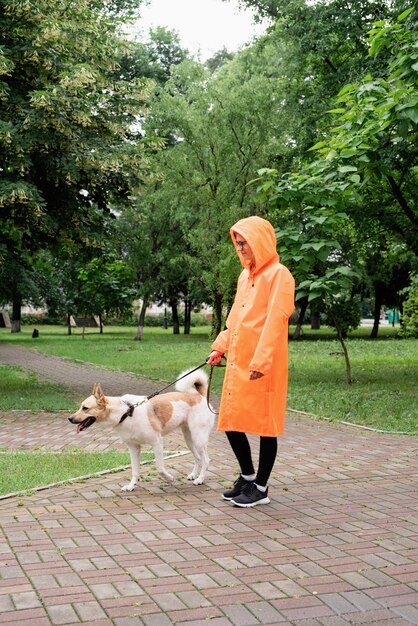 Giovane donna in impermeabile arancione che cammina con il suo cane in un parco