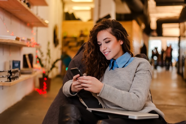 Giovane donna in interni moderni usando il suo telefono.