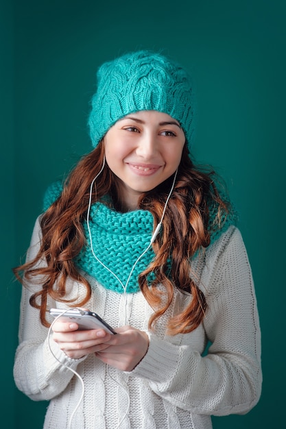 Giovane donna in maglia sciarpa e cappello ascoltando musica in cuffia