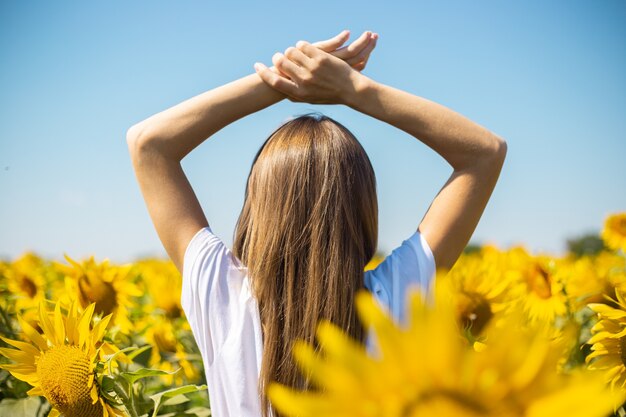 Giovane donna in maglietta bianca con le mani alzate su un campo di girasoli in una giornata di sole estivo.