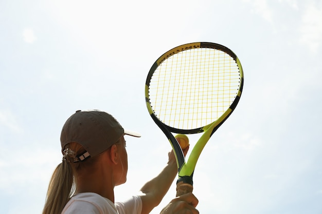 Giovane donna in maglietta bianca serve la pallina da tennis