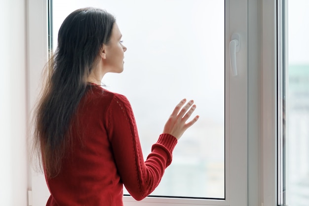 Giovane donna in maglione rosso guardando fuori dalla finestra