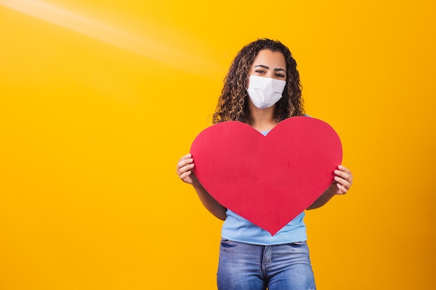 Giovane donna in maschera chirurgica che tiene un enorme cuore di carta con spazio per il testo.