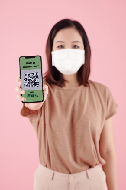 Giovane donna in maschera medica che mostra il codice qr che indica che il suo titolare è stato vaccinato