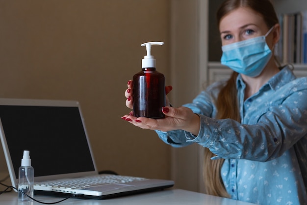 Giovane donna in maschera per disinfettare le superfici dei gadget sul suo posto di lavoro