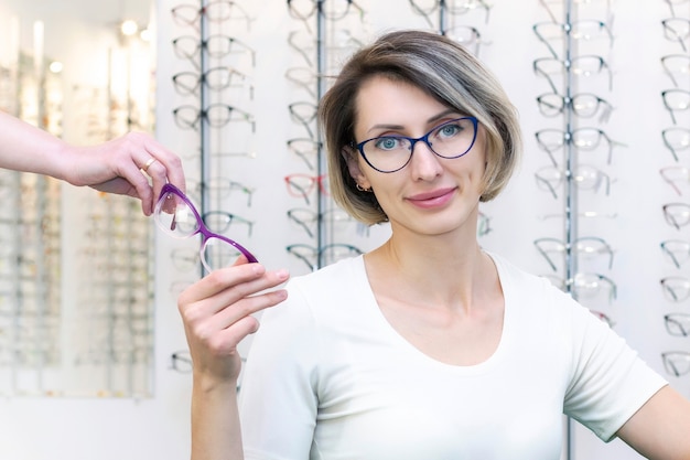 Giovane donna in negozio di ottica scegliendo nuovi occhiali con ottico. occhiali nel negozio di ottica. Una donna sceglie gli occhiali. Emozioni. Oftalmologia.