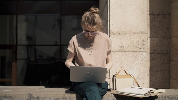 Giovane donna in occhiali da sole con il computer portatile che si prepara per l'esame all'esterno