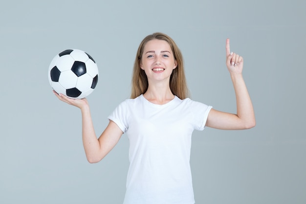 Giovane donna in pallone da calcio bianco della tenuta della camicia che indica un dito su.