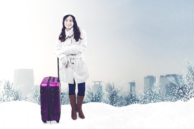 Giovane donna in piedi con i bagagli al parco nevoso