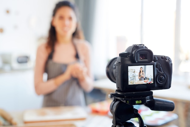 Giovane donna in piedi da sola nella sua cucina che riprende il tutorial sui prodotti da forno per il suo canale blog di cibo