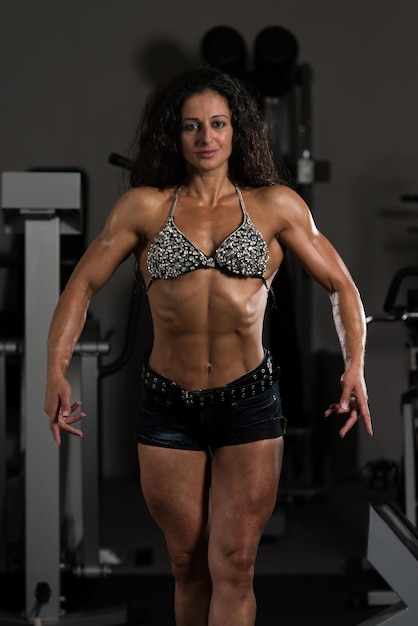 Giovane donna in piedi forte in palestra e flettendo i muscoli Muscoloso modello di fitness bodybuilder atletico in posa dopo gli esercizi