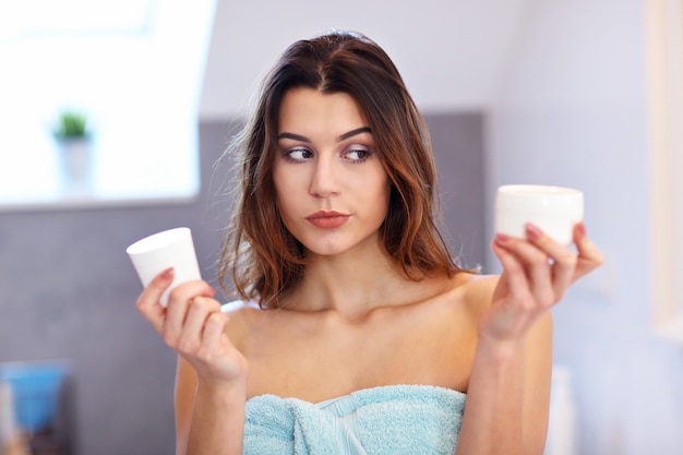 Giovane donna in piedi in bagno e applicando la crema per il viso al mattino