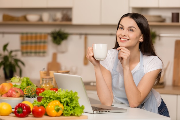 Giovane donna in piedi in cucina con il computer portatile